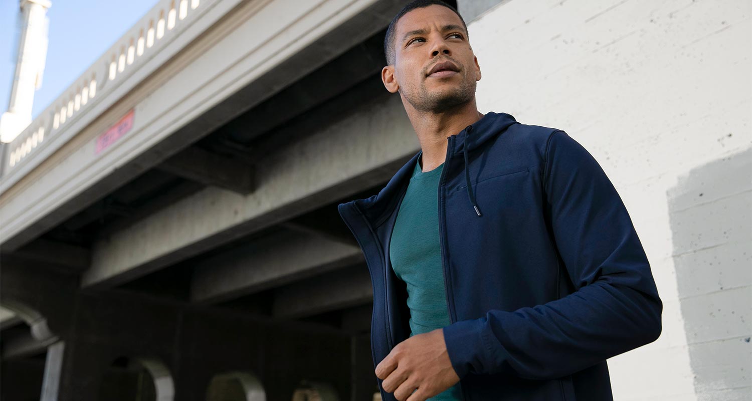 MPG male model outside under a bridge, wearing a navy blue jacket and green shirt