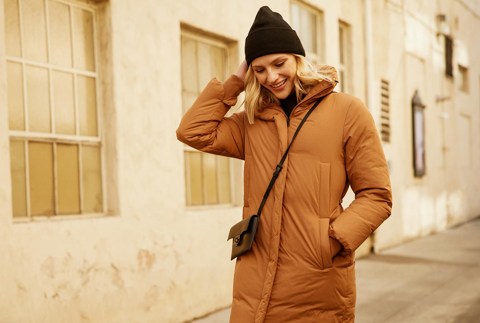 MPG female model looking happy, enjoying a walk outside in her camel colored down parka
