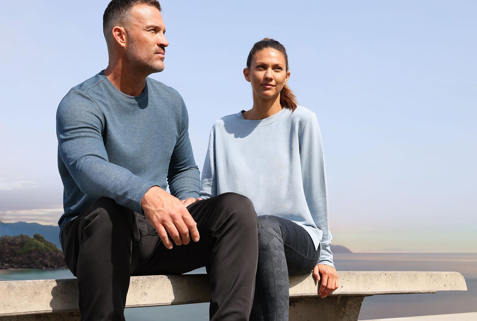 Mondetta man and woman modeling activewear sitting on a bench near the seaside