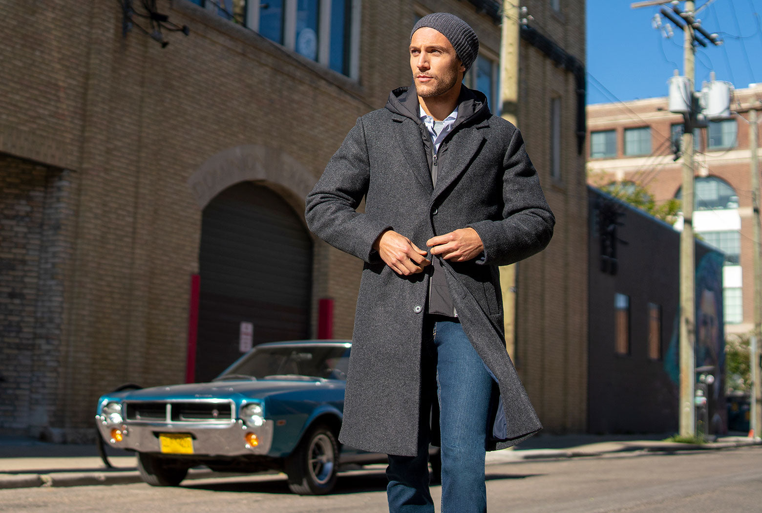 Modern Ambition male model crossing the street in a long grey coat, vintage sports car in the background